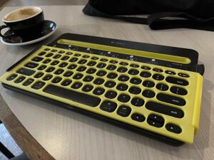 Yellow 3d printed keyguard being used with a black and yellow K480 wireless keyboard at a cafe
