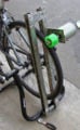 תמונה 3: תמונה מעט מטושטשת של יחידת הגנרטור המחוברת לתמוכות ומותקנת על מעמד האופניים. שימו לב שגלגל החיכוך יוצר קשר עם גלגל האופניים, אך ניתן לסובב אותו הרחק מנקודת הציר התחתונה, מה שמאפשר להסיר את האופניים